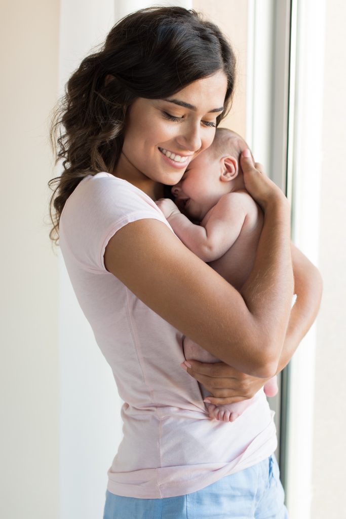 Mom Lovingly Hugging her baby by window on Breastfeeding School www.breastfeedingschool.com by Haydee Montemayor